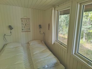 A room with a single bed, two wall-mounted lamps, a framed botanical illustration, and a window with a view of greenery. - Cozy holiday home in Hune near Blokhus (Hune)