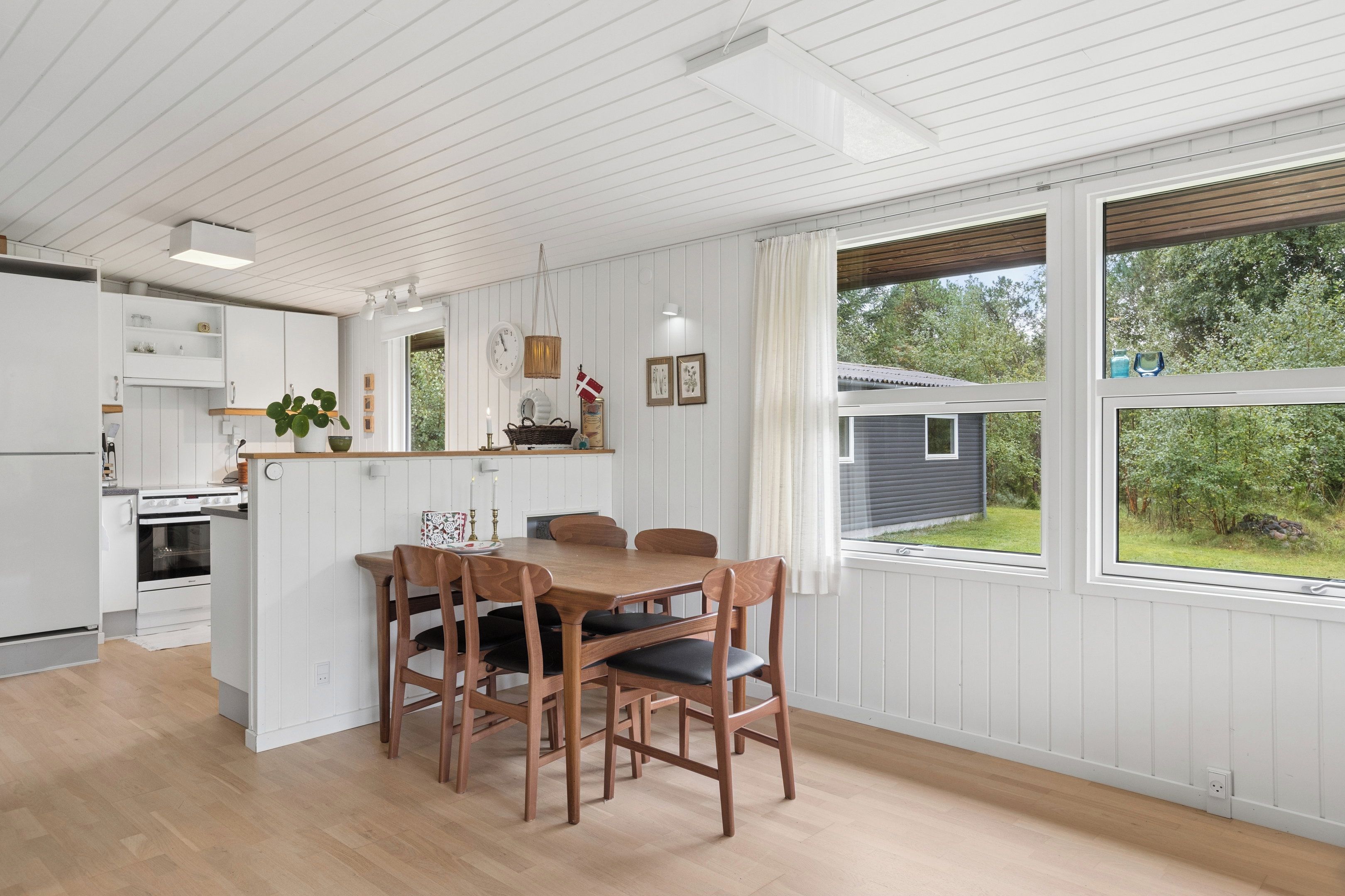 Eine moderne Küche mit weißen Schränken, ein Essbereich mit Holzkästen und große Fenster mit Blick ins Freie.
