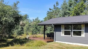 A single-story house with a covered porch, surrounded by a grassy yard and dense trees. - Cozy holiday home in Hune near Blokhus (Hune)