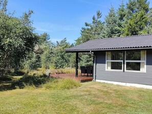 A single-story house with a covered porch, surrounded by a grassy yard and dense trees. - Cozy holiday home in Hune near Blokhus (Hune)