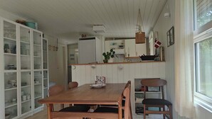 A dining area with a wooden table and chairs, a kitchen with white cabinets, and a window with curtains. - Cozy holiday home in Hune near Blokhus (Hune)