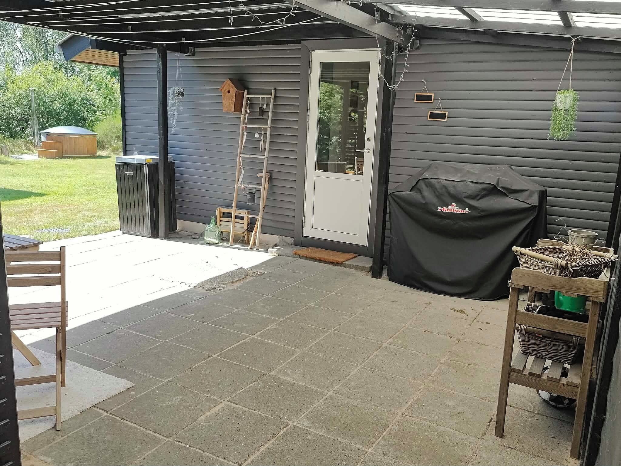 Un patio cubierto con una parrilla, una escalera de madera y un comedero para pájaros.