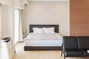 Ein Hotelzimmer mit einem Bett, einem Sessel, einem Nachttisch und einer Wand-Klimaanlage.