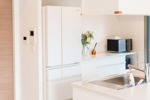 A modern kitchen with white cabinetry, a microwave, a sink, and a vase with flowers. - Aoba Residence AOZORA 1002 Near Dotonbori 3-Bedroom, 2 Bathrooms, 2 Toilets Premium Tower Residence (大阪市)