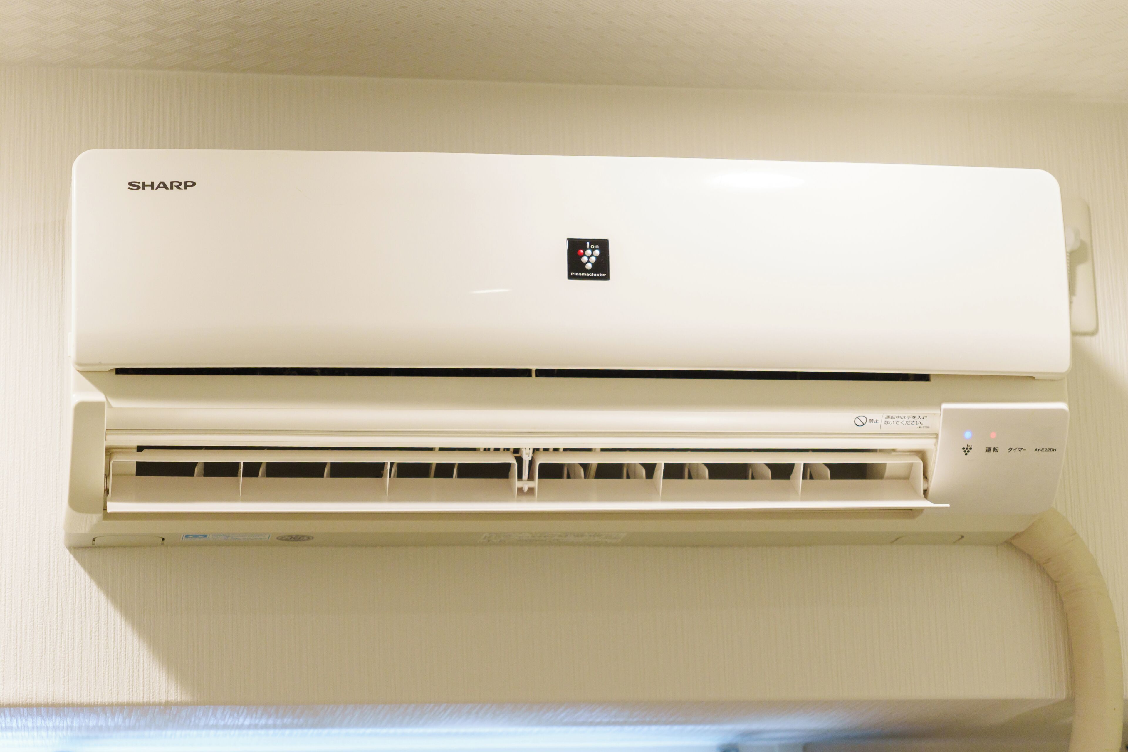 A white Sharp air conditioner unit mounted on a wall with a control panel on the right side.