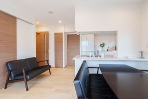 A modern living room with a black leather sofa, a dining table, and a kitchen area with a refrigerator and a vase of flowers. - Aoba Residence AOZORA 1002 Near Dotonbori 3-Bedroom, 2 Bathrooms, 2 Toilets Premium Tower Residence (大阪市)
