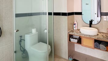 Une salle de bain avec une douche à parois de verre, des toilettes, un lavabo et un miroir.