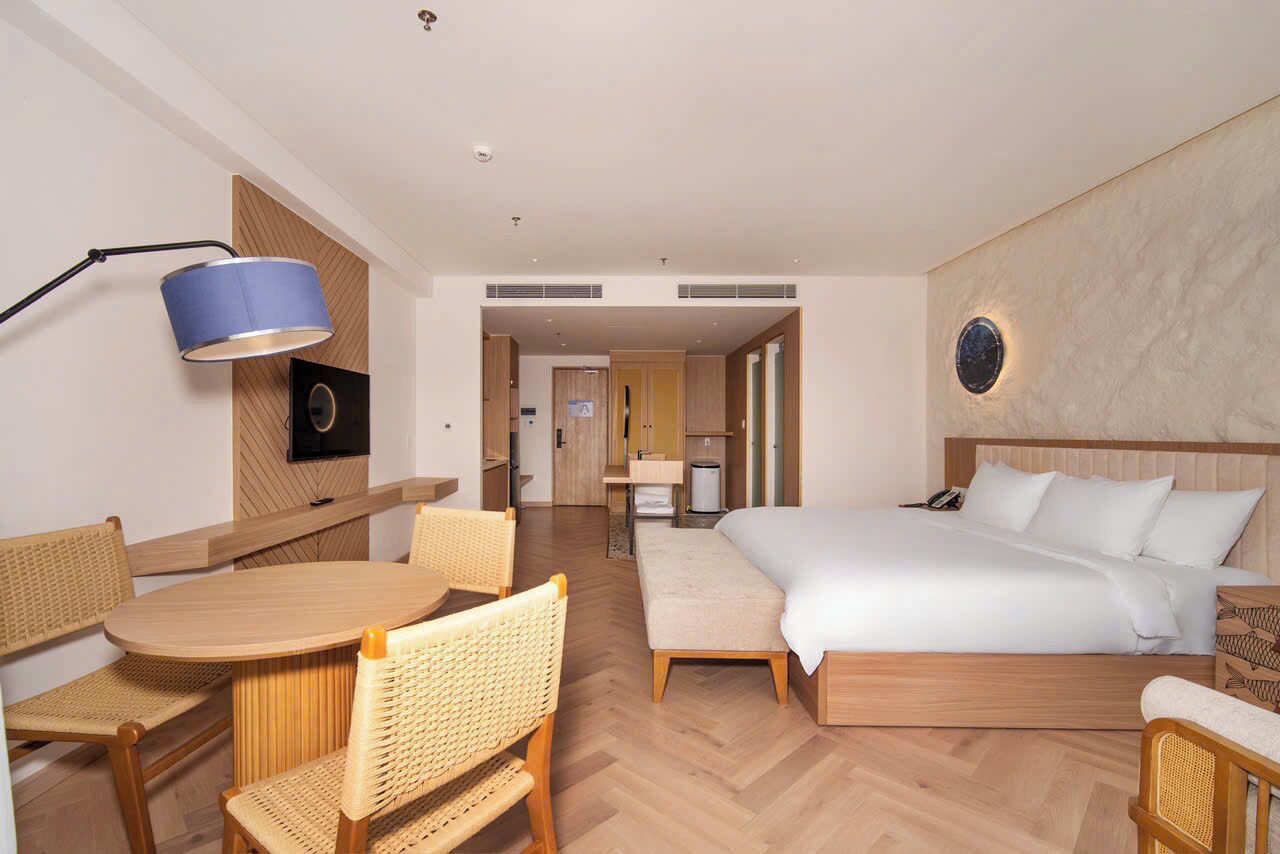 Une chambre d’hôtel comprenant un lit, un bureau avec des chaises, une lampe et un luminaire fixé au mur.