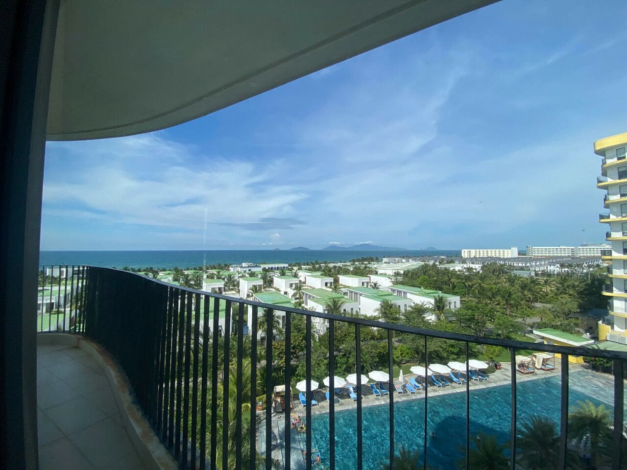 Un balcon offrant une vue sur une zone de villégiature, avec notamment une piscine et des bâtiments visibles au loin.