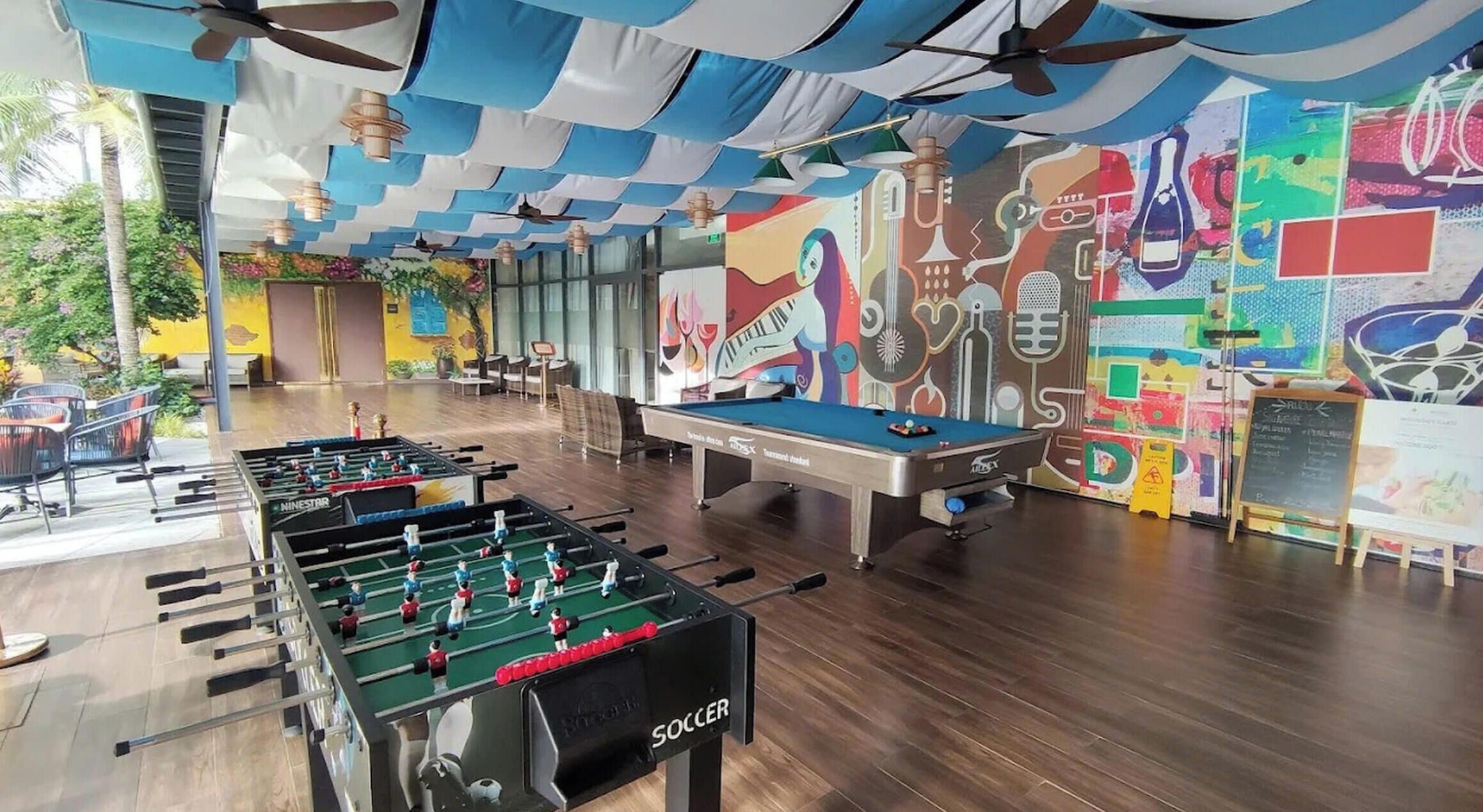 Ein Zimmer mit einer Tischfußballplatte, einem Billardtisch und einem Wandgemälde mit abstrakter Kunst.