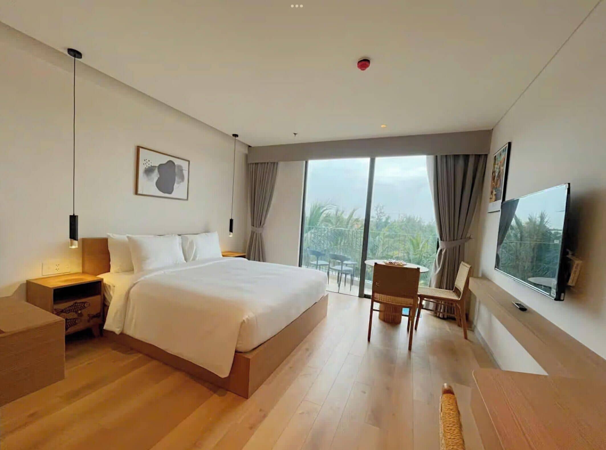 Una habitación de hotel moderna con una cama grande, televisión, zona de comedor y balcón con vistas.