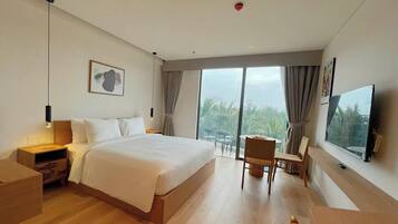 Una habitación de hotel moderna con una cama grande, televisión, zona de comedor y balcón con vistas.