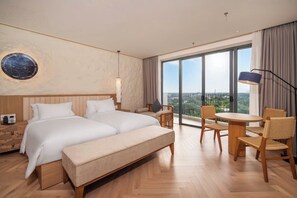 Habitación de hotel con una cama grande, un escritorio con sillas, una mesa redonda y vistas a la ciudad.