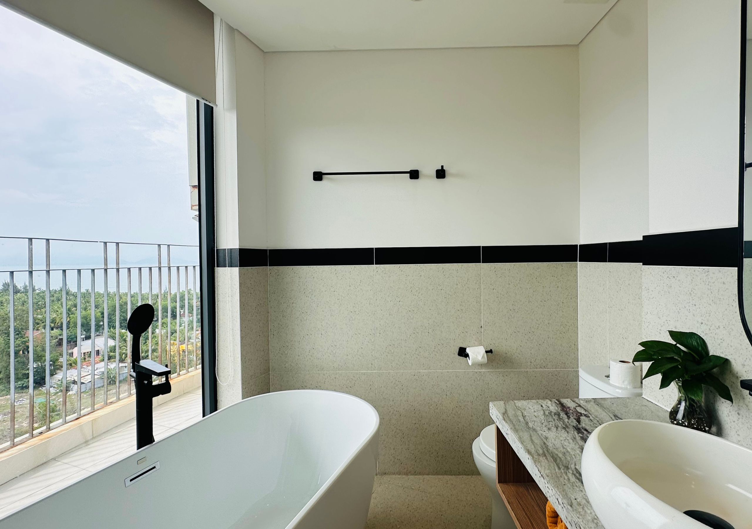 Ein modernes Badezimmer mit Badewanne, Toilette und Waschbecken. Ein Balkon bietet Blick auf die Stadt.