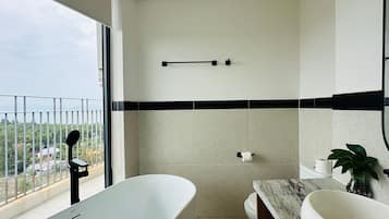 A modern bathroom with a bathtub, a toilet, and a sink. There is a balcony with a view of the city.