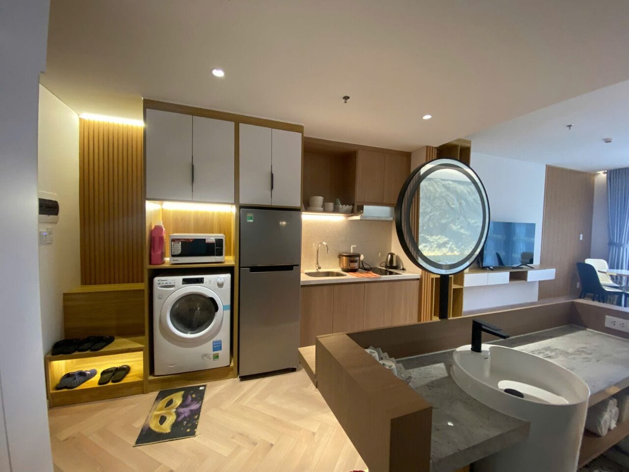 A compact hotel room with a kitchenette, a washing machine, a built-in oven, a microwave, and a large mirror.