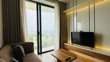 A modern hotel room with a sofa, a coffee table, a TV, and a balcony with curtains.