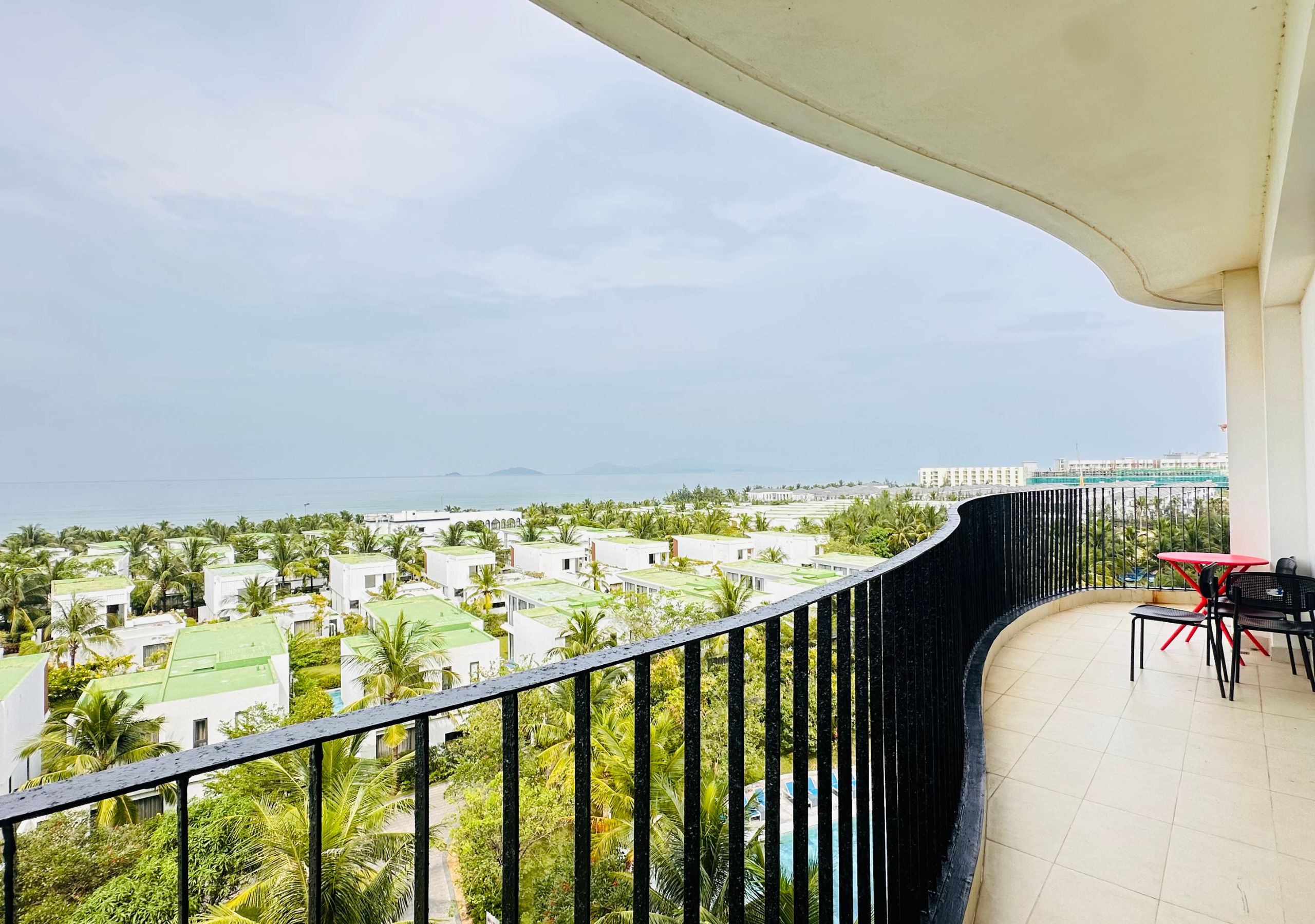 Un balcón con vista a una zona residencial, una piscina y una masa de agua distante.