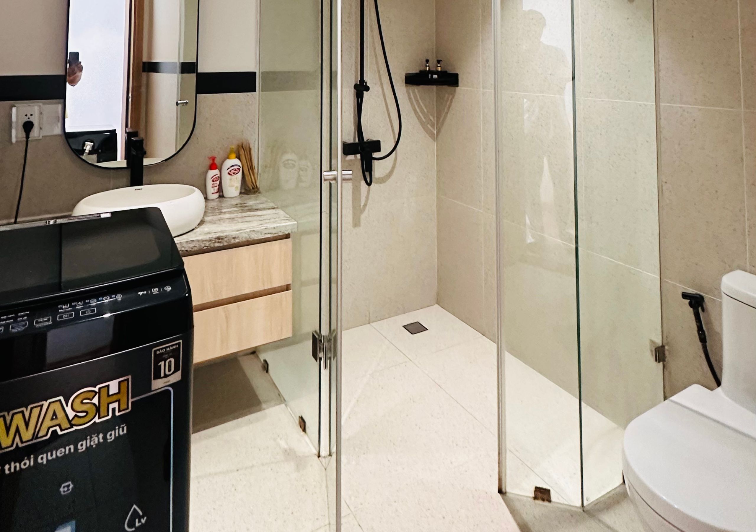 Un baño moderno con cabina de ducha de vidrio, inodoro blanco y lavabo con espejo arriba.