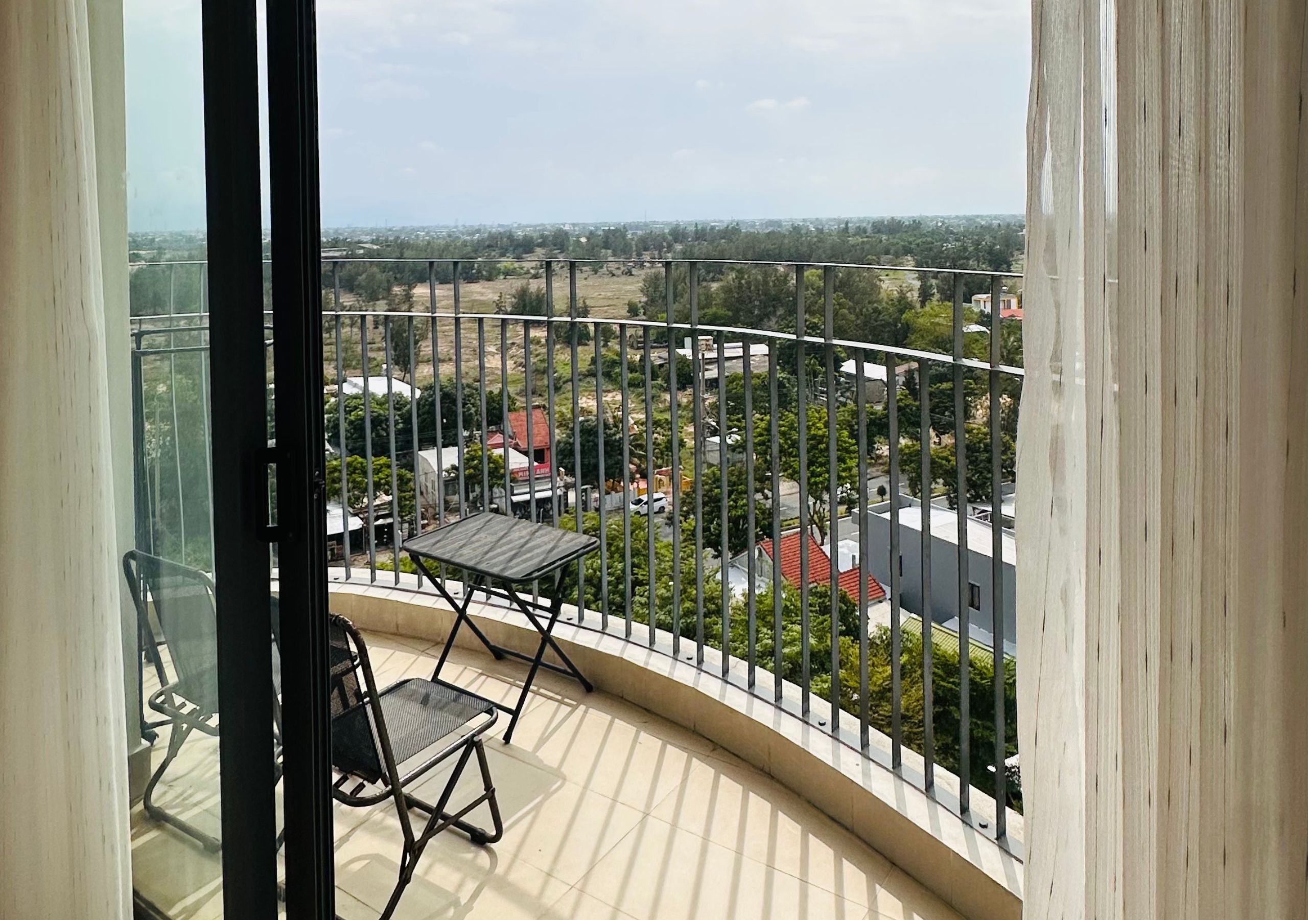 A balcony with a table and chairs, overlooking a residential area with houses and greenery.