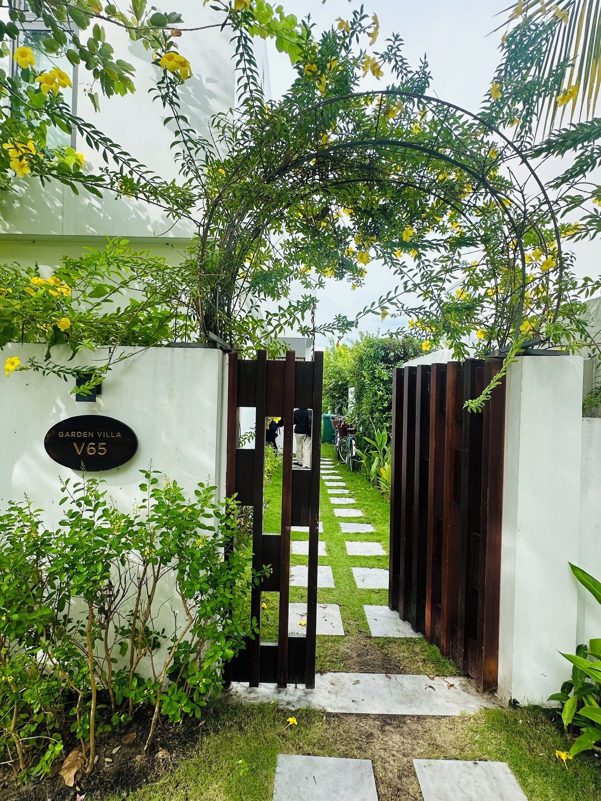 Una entrada con puerta y un camino que lleva a un edificio con la leyenda 'Garden Villa V65'.