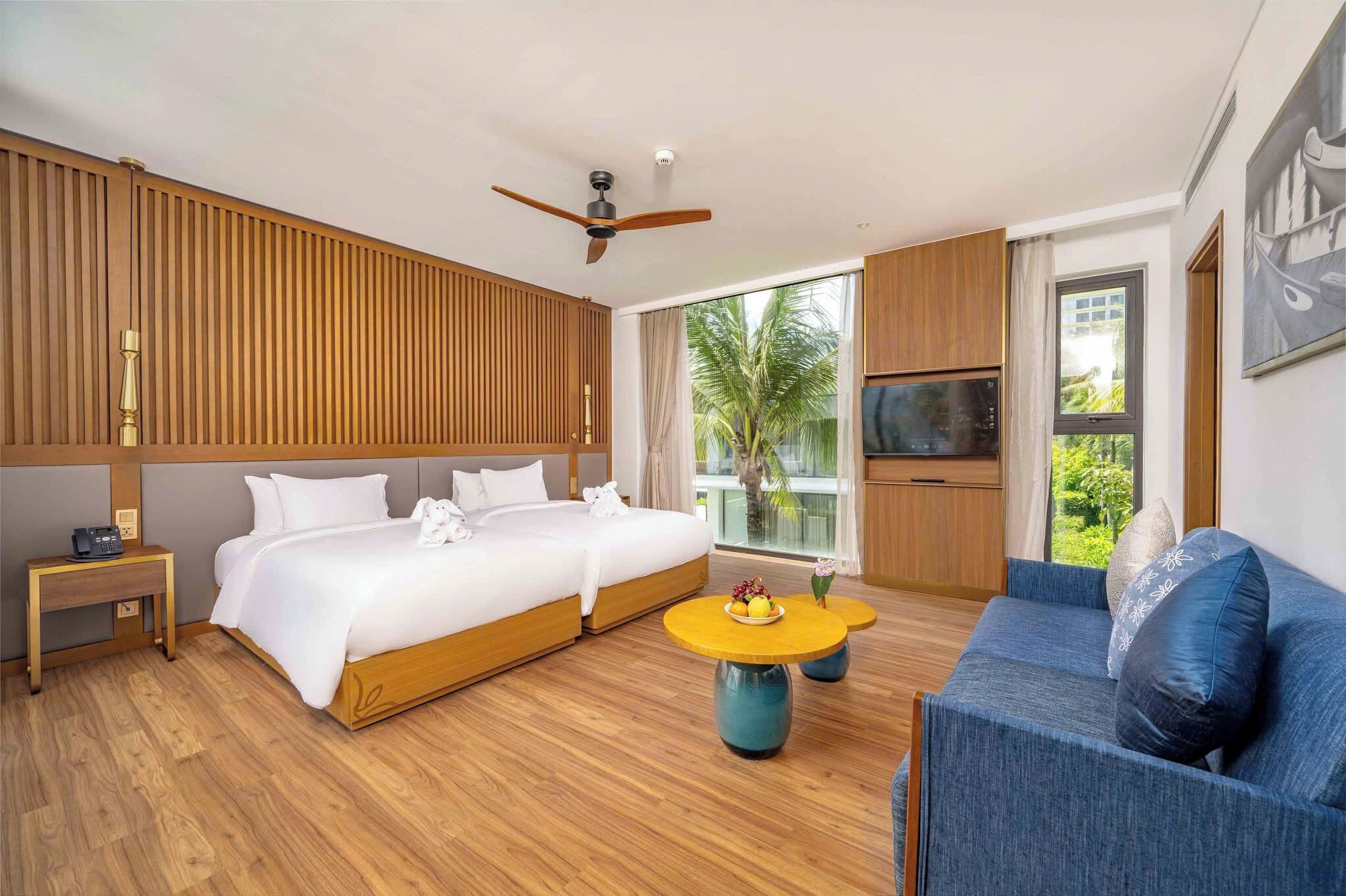 Une chambre d’hôtel avec un grand lit, un canapé, une télévision et un balcon donnant sur des palmiers.