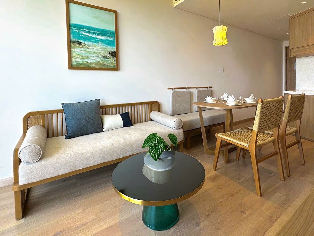A modern living room with a sofa, a dining table with chairs, a round coffee table, and a painting of a beach scene on the wall.
