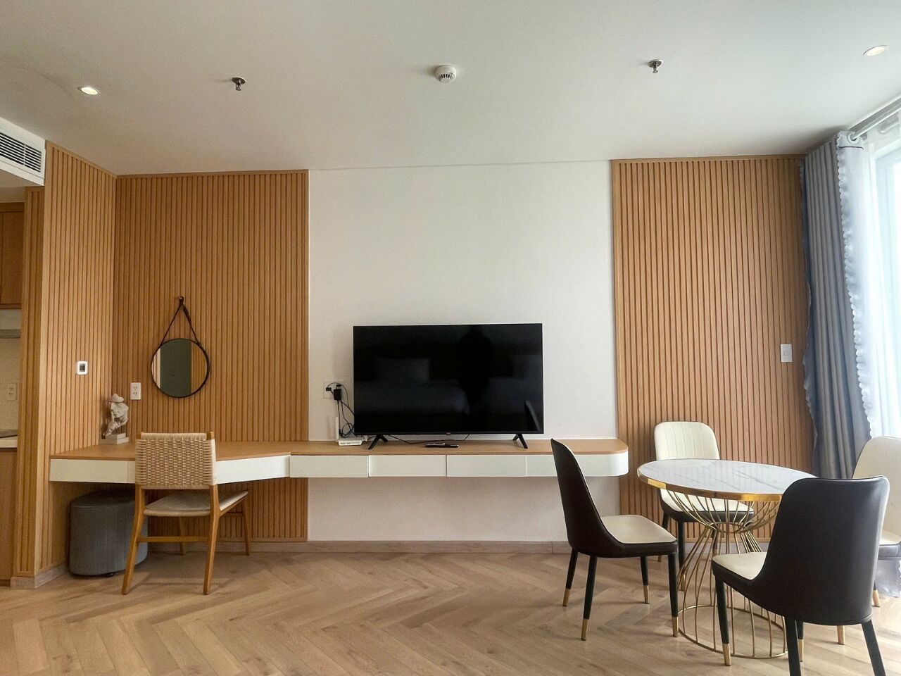 Una habitación de hotel moderna con televisor de pantalla plana, un rincón de comedor con una mesa redonda y sillas, y una zona de estar con un sofá y una butaca.