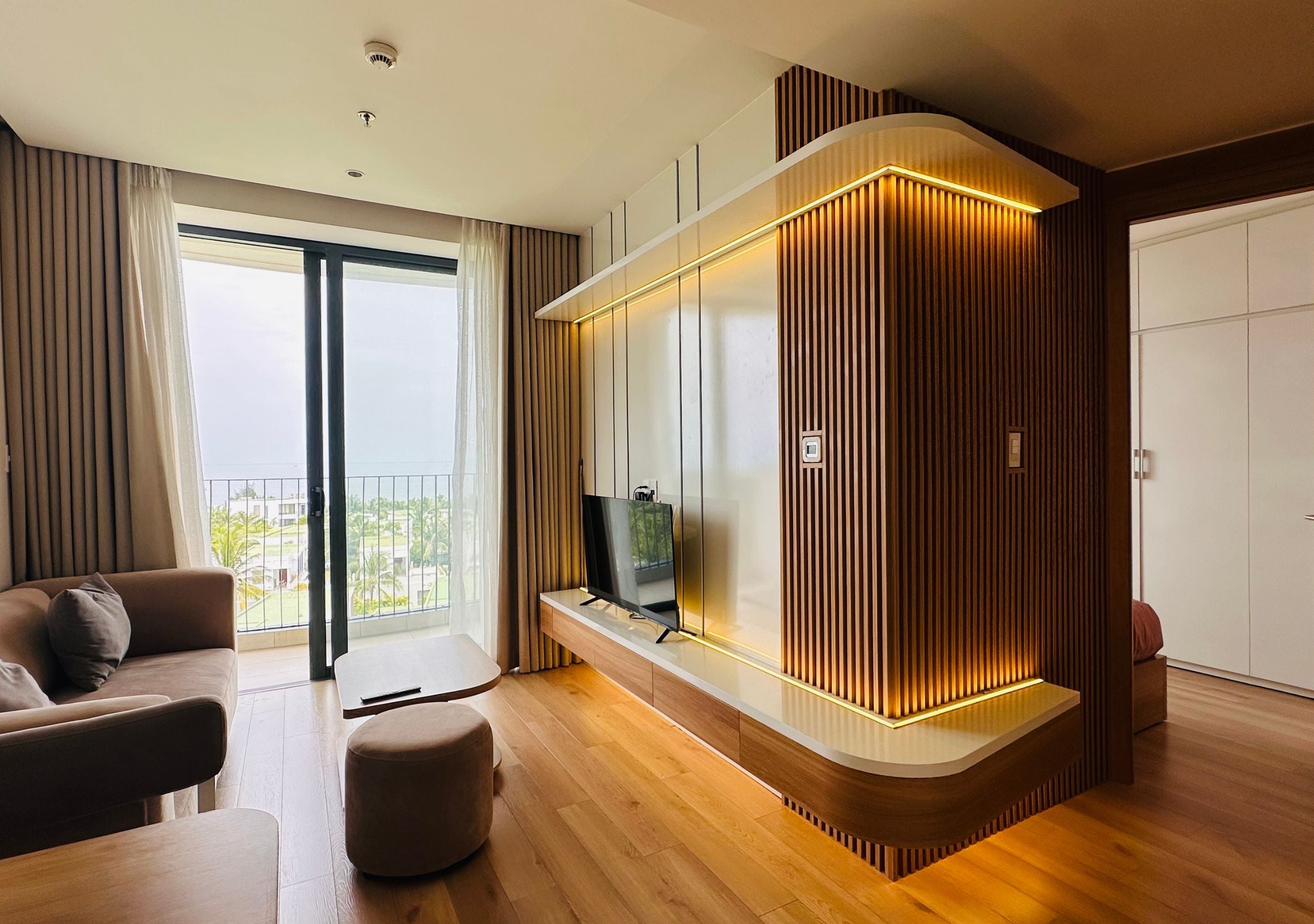 Un soggiorno moderno con una grande TV a schermo piatto, pannelli in legno, un divano e un balcone con tende.
