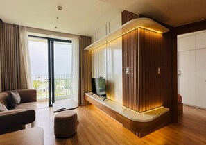 A modern living room with a large flat-screen TV, wooden paneling, a sofa, and a balcony with curtains. - Hoi An Sea Breeze Resort (Hoi An)