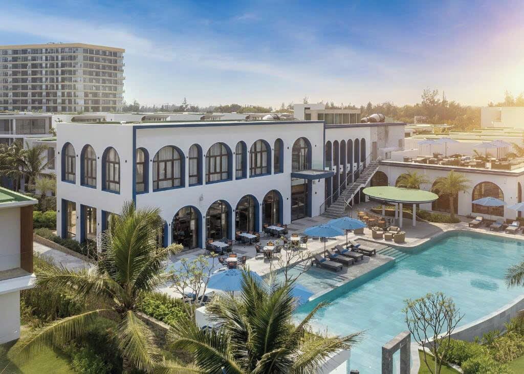 Un hôtel doté d’une piscine, d’un espace extérieur aménagé et d’un grand bâtiment aux fenêtres en arc de cercle.