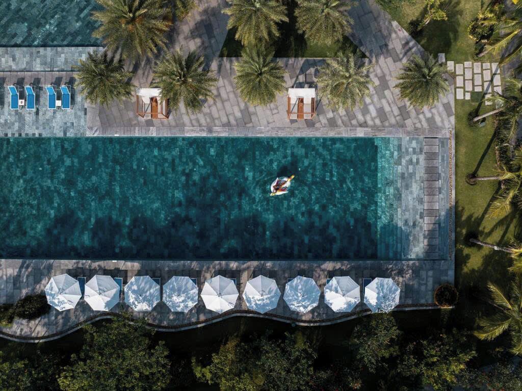 Una vista aerea di un resort con piscina, lettini, ombrelloni e palme.