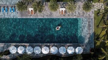Una vista aerea di un resort con piscina, lettini, ombrelloni e palme.