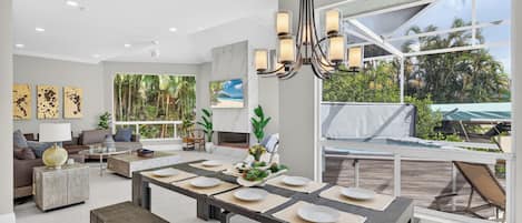 A modern living room with a dining area, large windows, and tropical decor.