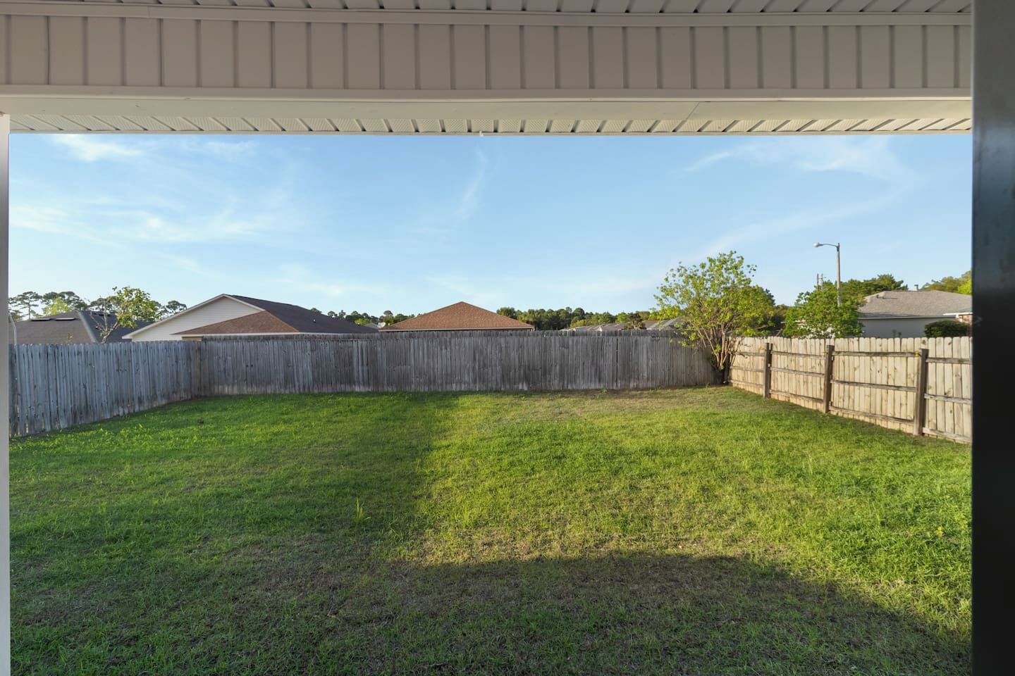 A backyard with a wooden fence, a lawn, and a house in the background.