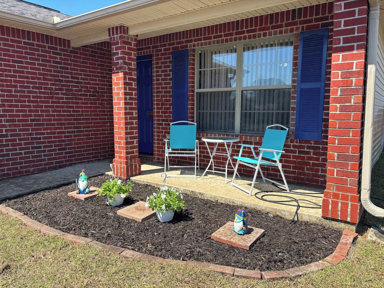 Une maison en briques dotée d’un patio comprenant une table et des chaises, le tout entouré de plantes en pot.