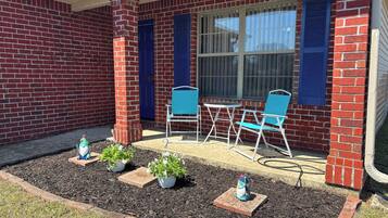 Une maison en briques dotée d’un patio comprenant une table et des chaises, le tout entouré de plantes en pot.