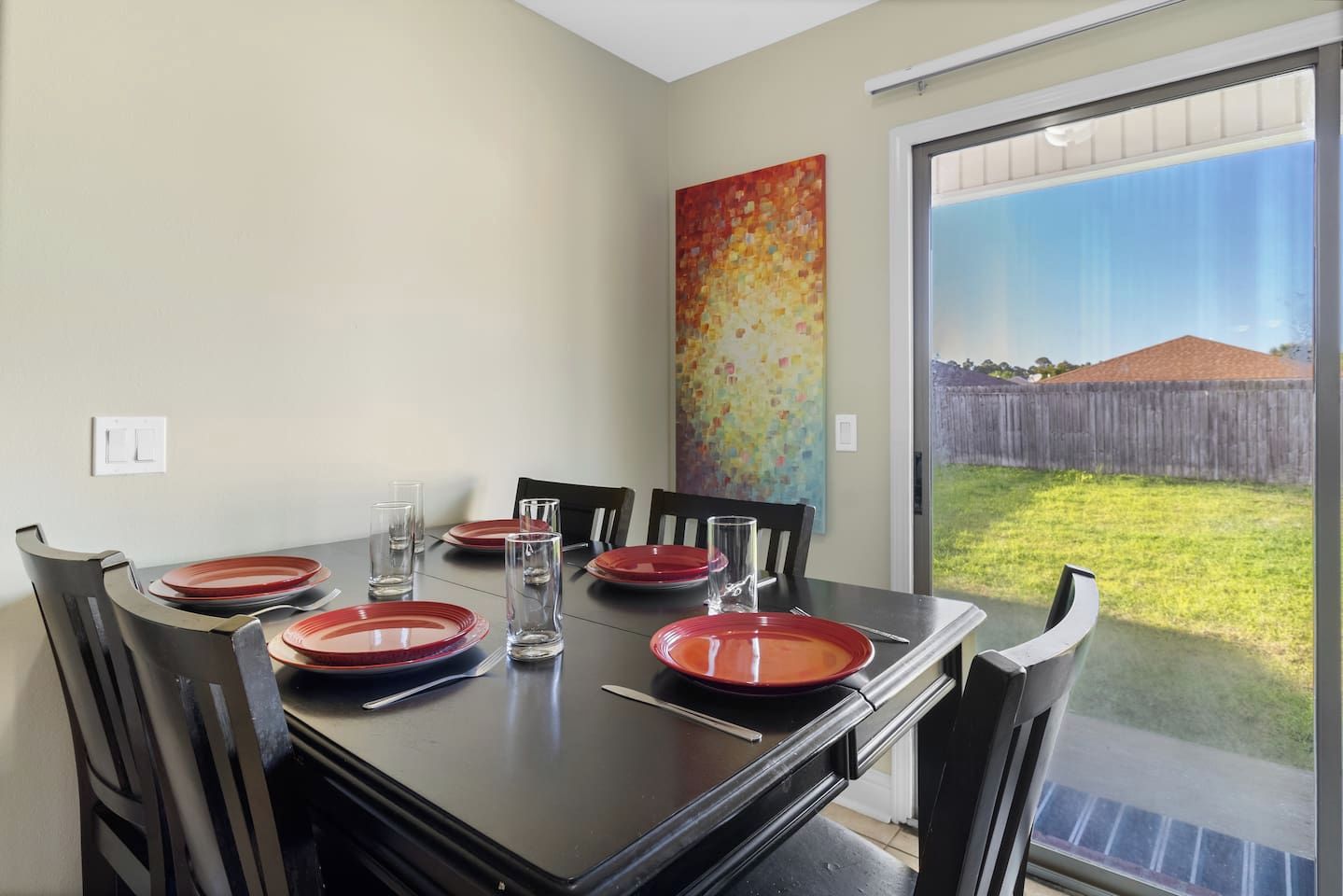 A dining area with a table set for four, chairs, and a view of a backyard through a sliding glass door.