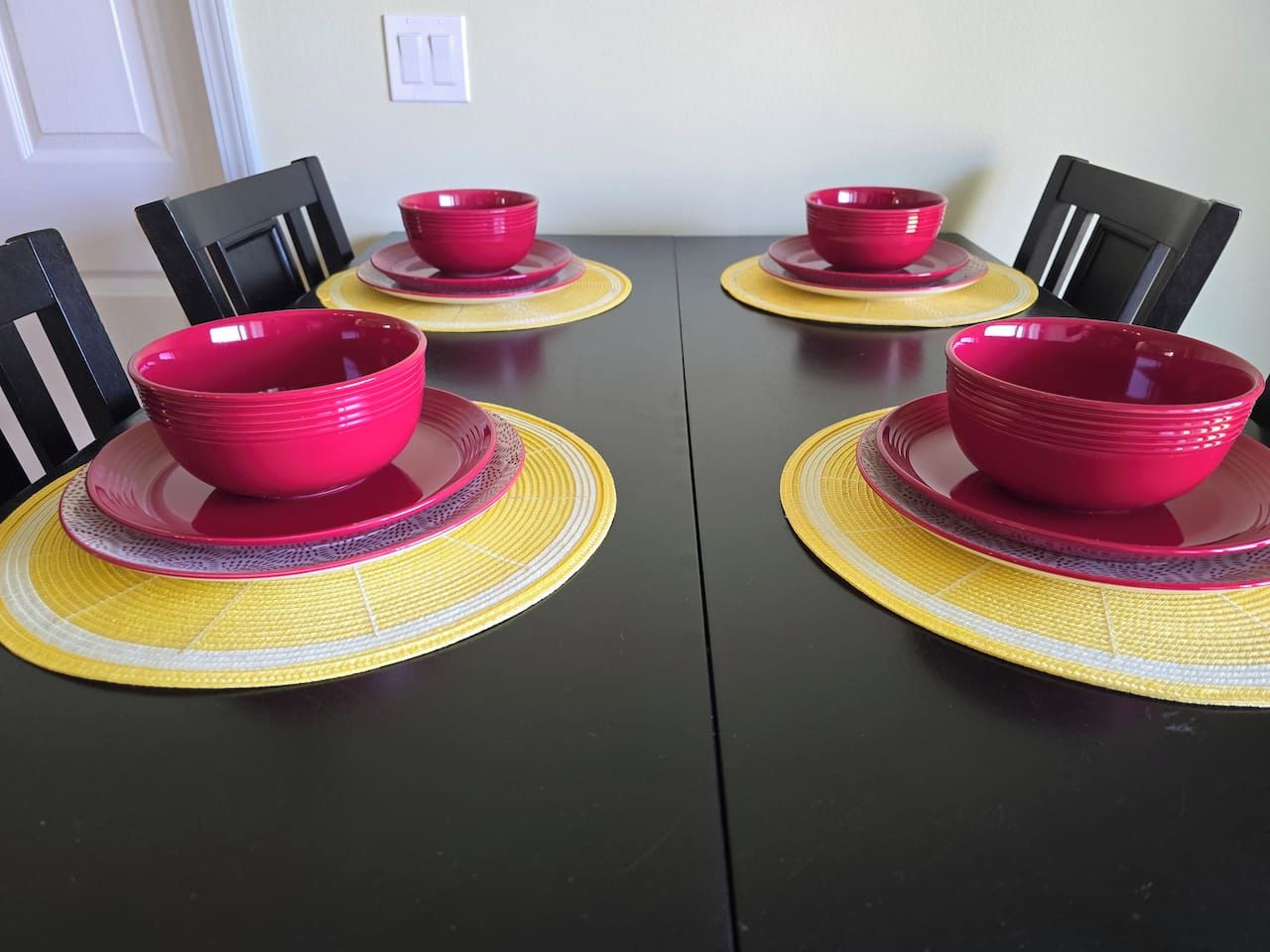 A dining table with four red bowls and yellow placemats.