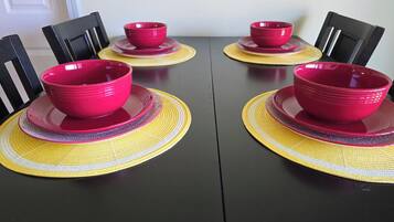 A dining table with four red bowls and yellow placemats.