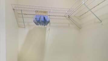 Una habitación con una puerta blanca, un tendedero metálico, un estante blanco con ropa doblada y una cuna infantil gris.