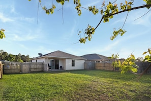 Ein Wohnhaus mit überdachter Terrasse, einem eingezäunten Garten und einer Satellitenschüssel.
