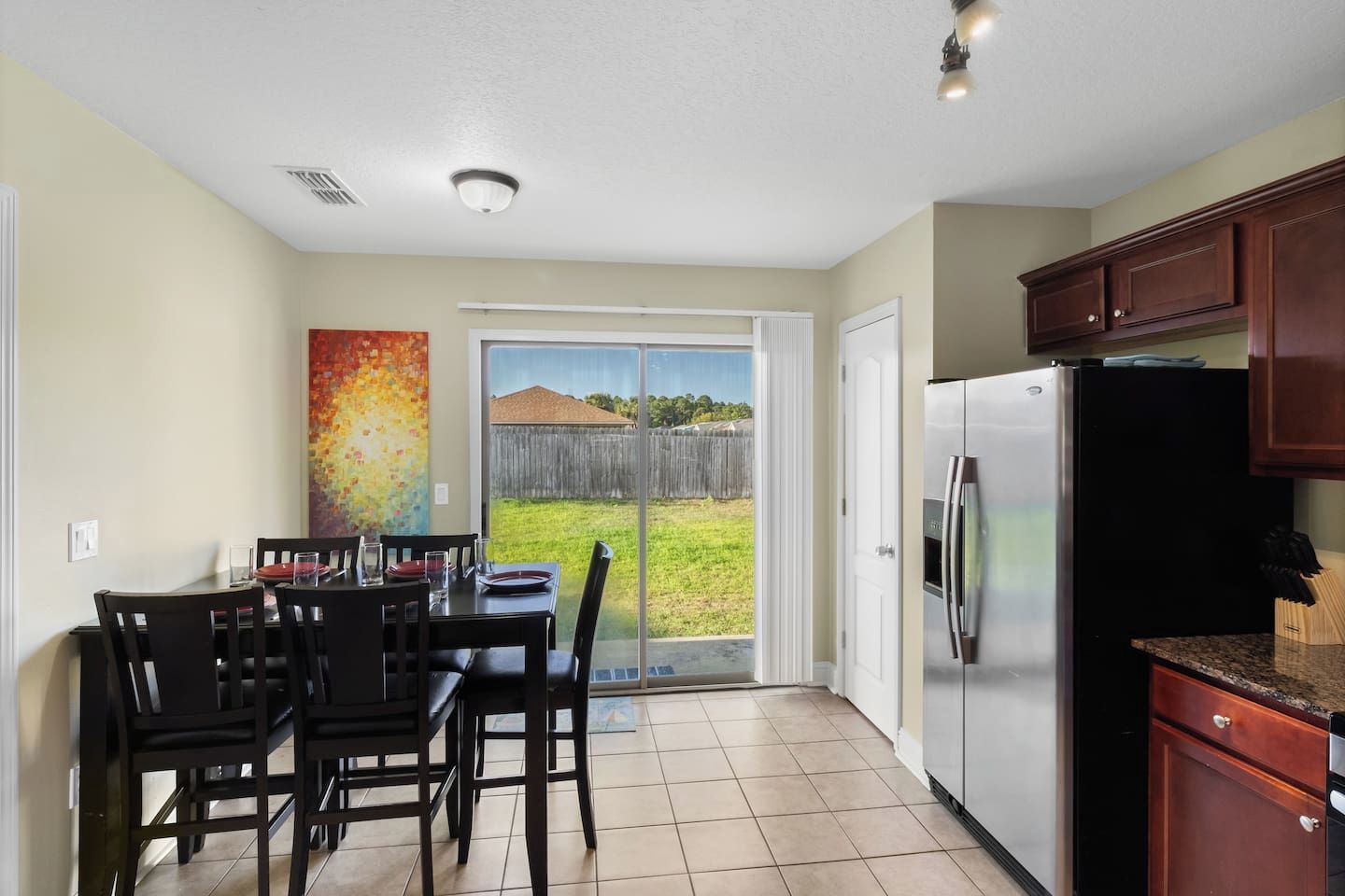 A kitchen with a sliding glass door leading to a backyard, a dining table with chairs, and a refrigerator.