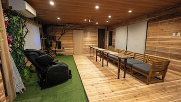 A room with a massage chair, a wooden table with chairs, and a green artificial turf area.