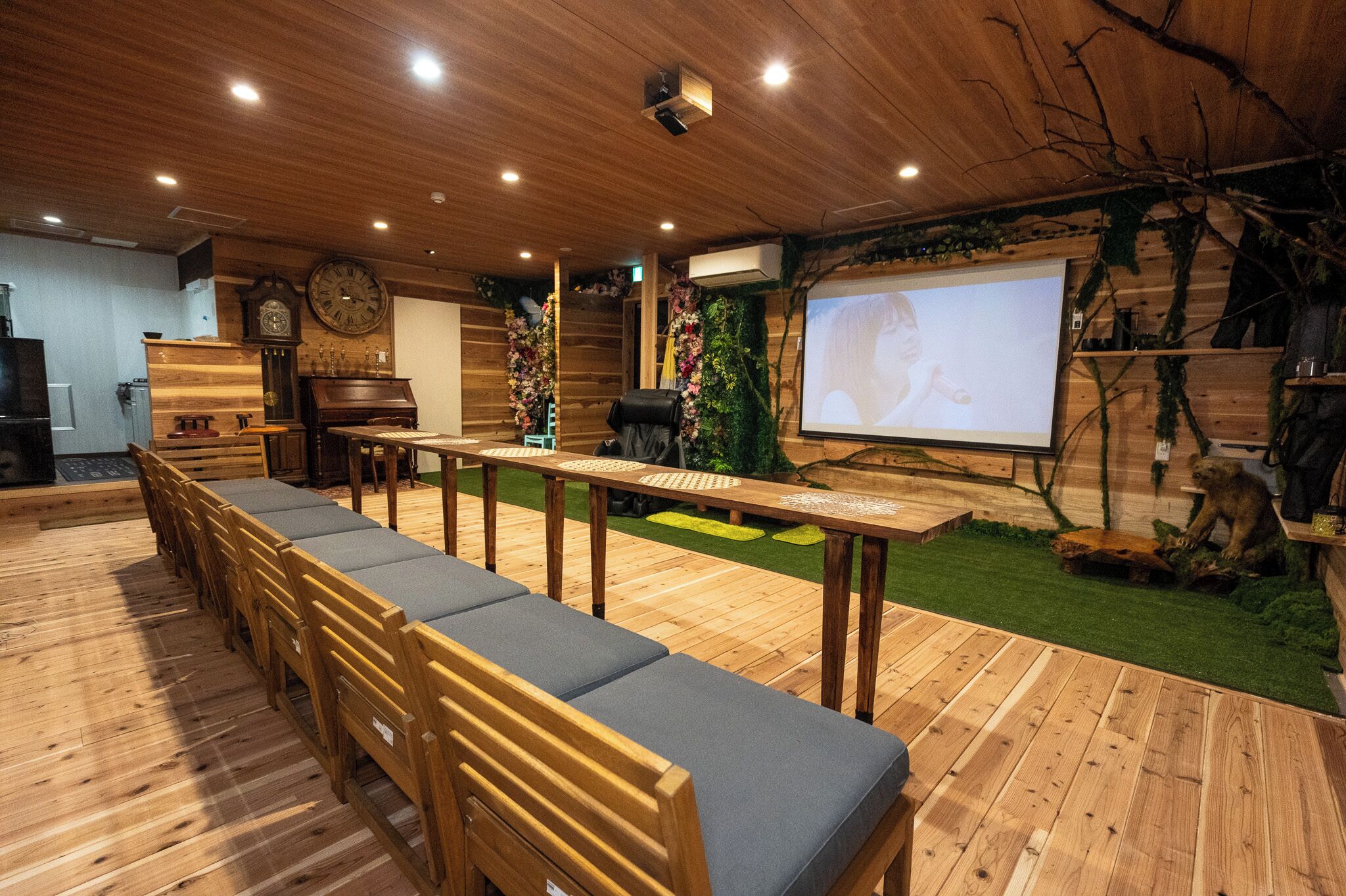 A room with a long wooden table, chairs, a projector screen, and a clock on the wall.
