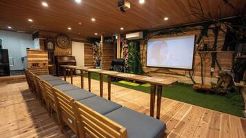 A room with a long wooden table, chairs, a projector screen, and a clock on the wall.