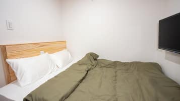 A single bed with a wooden headboard, white pillows, and a green blanket.