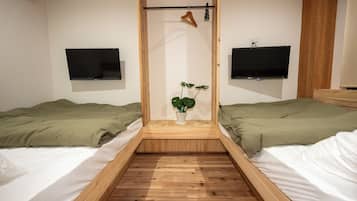 A room with two beds, a wooden floor, a plant in a vase, and two mounted TVs.