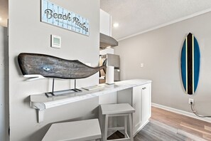 Eine Küche mit weißer Arbeitsplatte, Wanddeko in Form eines Fisches, einem Surfbrett und einem Schild mit der Aufschrift 'Beach Rules'.