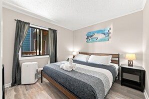 Ein Schlafzimmer mit einem Bett, einem Nachttisch, einer Lampe, einem Heizgerät und einem Fenster mit Vorhängen.